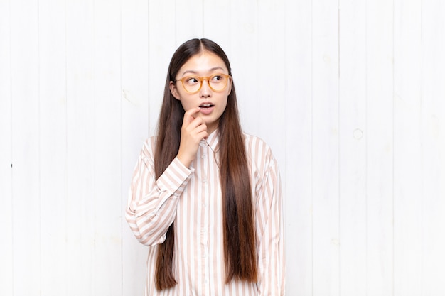 Asiatische junge Frau mit überraschtem, nervösem, besorgtem oder verängstigtem Blick, der zur Seite in Richtung Kopierraum schaut