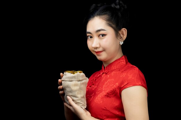 Asiatische junge Frau rotes Kleid traditionelles Cheongsam hält eine Goldmünze in einem Sack China Girl
