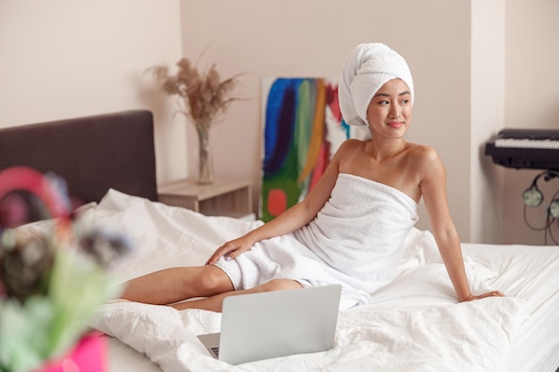 Asiatische junge Frau sitzt zu Hause mit Notizbuch auf dem Bett