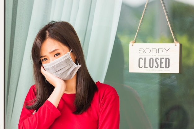 Asiatische junge Frau trägt eine Gesichtsmaske und schützt sie mit einem traurigen Hinweisschild