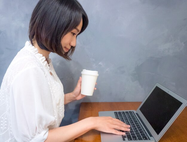 Asiatische junge Frau trinkt vor Laptop