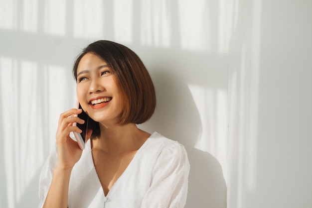 Asiatische junge Frau über isolierter weißer Wand, die ein Gespräch mit dem Handy führt