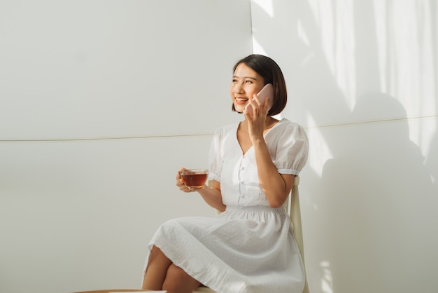 Asiatische junge Frau über isolierter weißer Wand, die ein Gespräch mit dem Handy führt