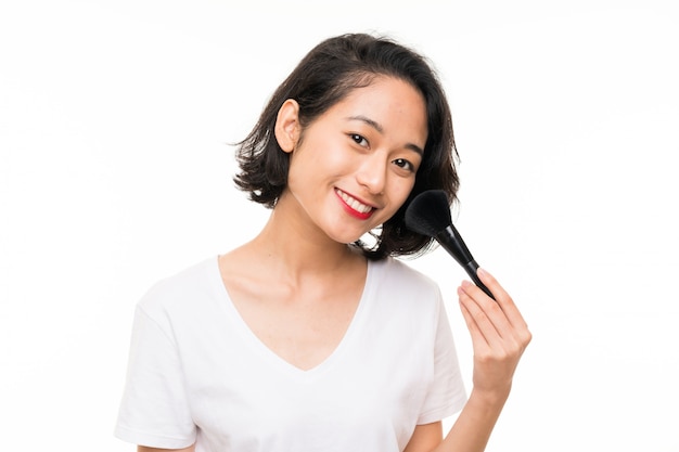 Asiatische junge Frau über lokalisierter Wand mit Make-upbürste