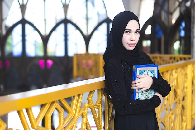 Asiatische junge muslimische frau tragen hijab schwarzes kleid, das koran, in moschee hält.