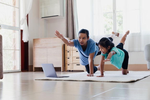 Asiatische junge Mutter und ihre Tochter, die zusammen zu Hause Stretching-Fitness-Übungen machen. Eltern, die das Kind unterrichten, trainieren, stark zu sein und die körperliche Gesundheit und das Wohlbefinden im Alltag zu erhalten.