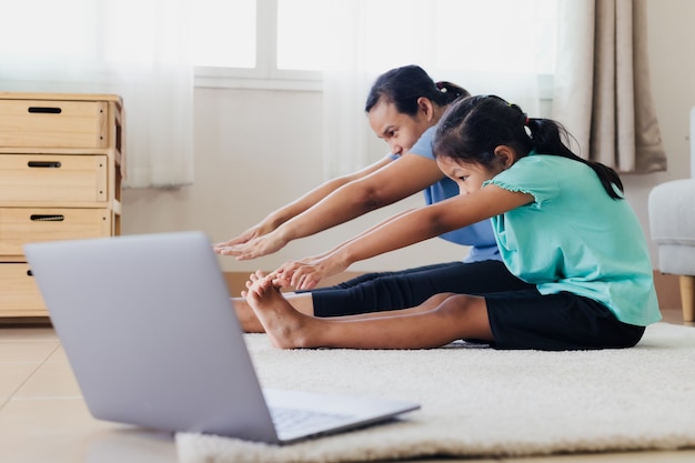 Asiatische junge Mutter und ihre Tochter, die zusammen zu Hause Stretching-Fitness-Übungen machen. Eltern, die das Kind unterrichten, trainieren, stark zu sein und die körperliche Gesundheit und das Wohlbefinden im Alltag zu erhalten.