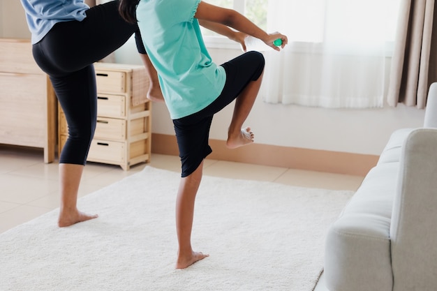 Asiatische junge Mutter und ihre Tochter machen Stretching-Fitness-Yoga und verwenden die Flasche Wasser, um zu Hause im Alltag zusammen Hanteln zu sein.