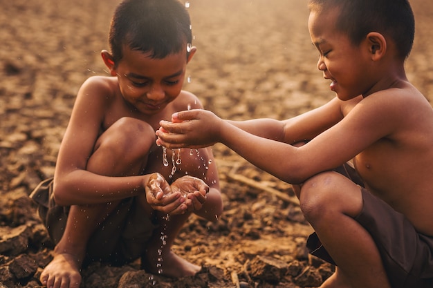 Asiatische Jungen aus der Region halten Wasser mit der Hand an trockenem, rissigem Land