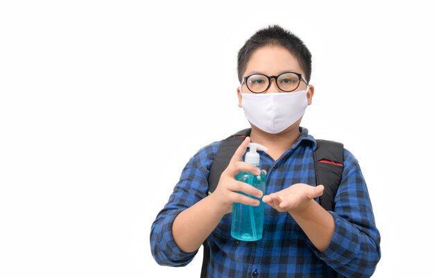 Asiatische Jungenstudenten tragen Maske, die Alkoholgelflasche lokalisiert auf Weiß hält