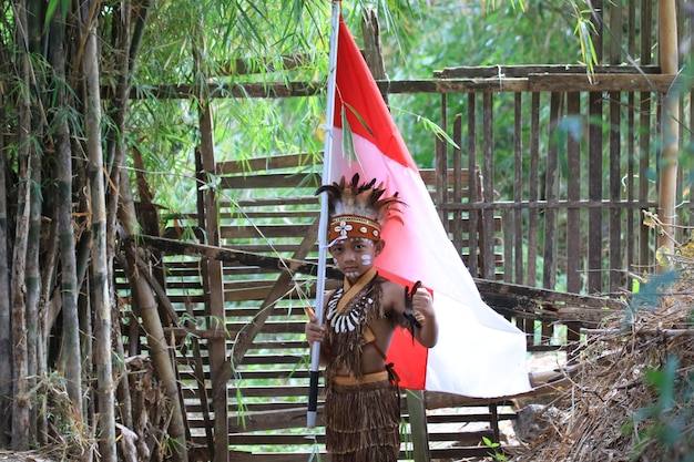 ASIATISCHE KINDER, DIE TRADITIONELLE KLEIDUNG VON PAPUA TRAGEN UND INDONESISCHE FLAGGE TRAGEN