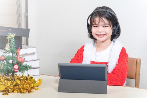 Asiatische Kinder kleines Mädchen kleiden Weihnachten Santa Claus im Chat mit Freunden auf digitalem Tablet. Weihnachtsferienkonzept Stockfotos