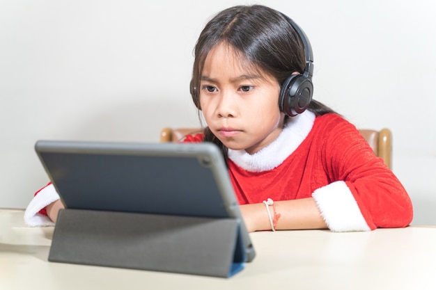 Asiatische Kinder kleines Mädchen kleiden Weihnachten Santa Claus im Chat mit Freunden auf digitalem Tablet. Weihnachtsferienkonzept Stockfotos