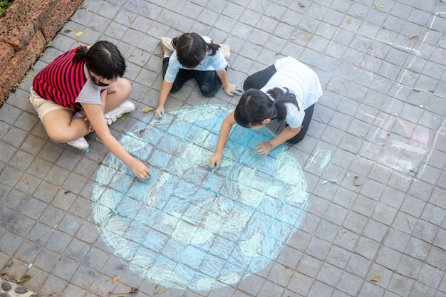 Asiatische Kinder spielen draußen. Kindermädchen zeichnet eine Planetenkugel mit einer Weltkarte farbiger Kreide auf dem Bürgersteig, Asphalt. Erde, Friedenstag-Konzert.