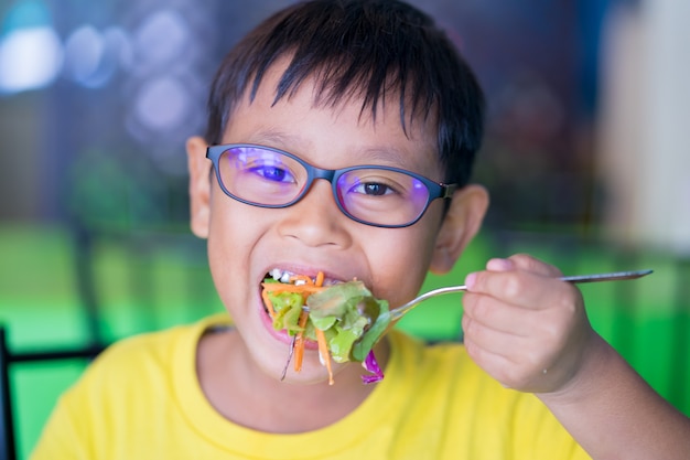 Asiatische Kinder tragen Gläser mit dem blauen Licht, das köstliche Salate im Restaurant blockiert und isst