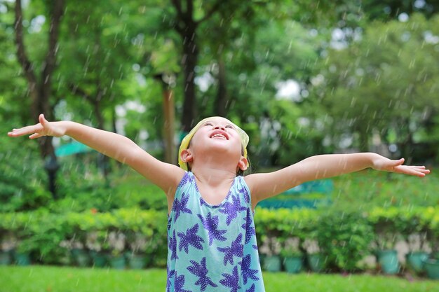 Asiatische kindermädchen-abnutzungs-plastiktasche auf dem kopf, der spaß hat, mit regen im garten zu spielen