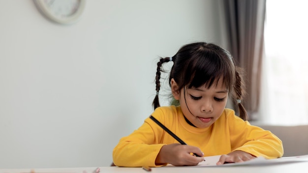 Asiatische Kinderschülerin zurück in die Schule oder Kindermädchen lächeln, schreiben Sie eine Notiz oder zeichnen Sie mit Bleistift und lesen Sie auf einem Computertablett, während Sie Hausaufgaben machen, um neue Ideen zu denken oder Menschen von zu Hause aus zu lernen