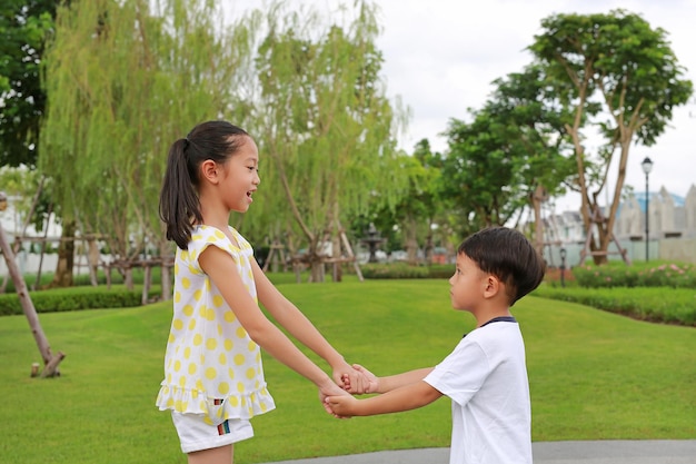 Asiatische kleine Jungen und Mädchen mit Hand in Hand beim gemeinsamen Spiel im Garten Asiatische Kinder im grünen Park