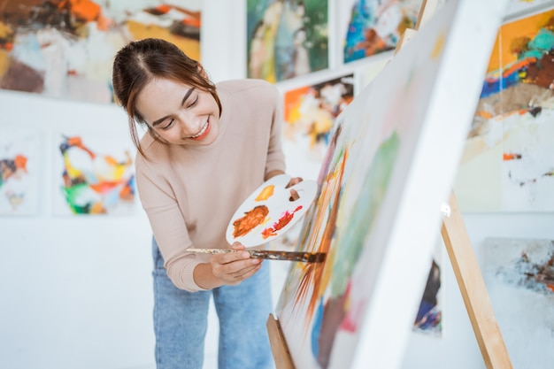 Asiatische Künstlerin, die auf Leinwand malt und einige Kunstprojekte in ihrer Atelierwerkstatt durchführt