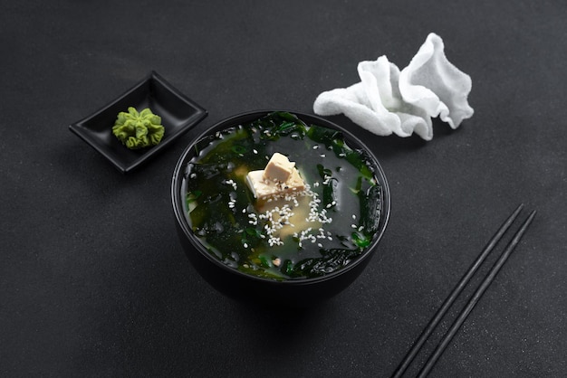 Asiatische Lebensmittelsuppe auf schwarzem Hintergrund in einer schwarzen Schüsselsuppe mit Draufsicht der Reischips