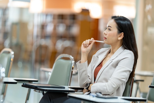 Asiatische Lehrerin, die sich in der Universitätsbibliothek Notizen vom Tablet macht