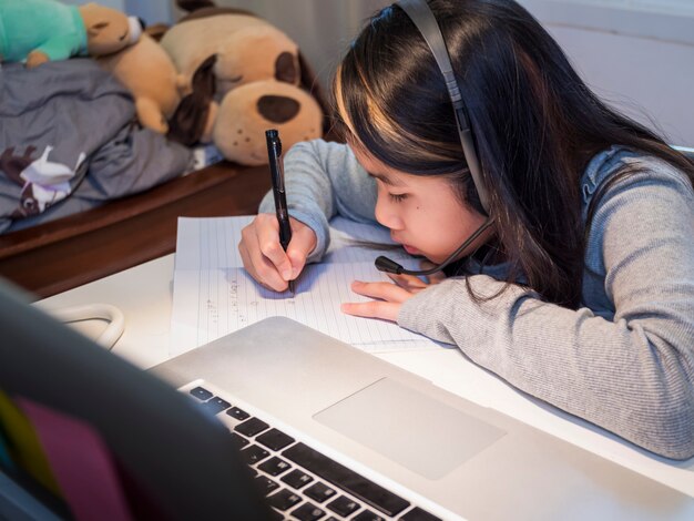 Asiatische Mädchen lernen online mit Laptop Kind tragen Headset-Schreiben im Notebook-Lernen mit Internet-Unterricht in Quarantäne Schüler lernen mit Internet-Online-Klasse von der Schule Covid19