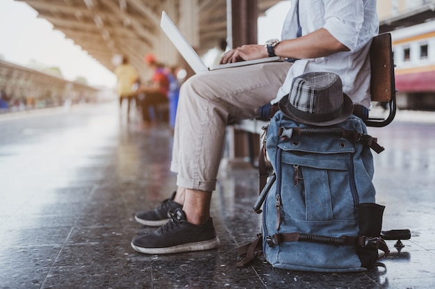 Asiatische Männer benutzen ihren Laptop, um zu arbeiten, während sie darauf warten, in den Zug einzusteigen, um zu reisen. Urlaub, Reise, Reise und Sommer Reisekonzept.