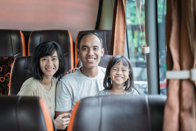 Asiatische Mama und Papa lächeln in die Kamera, während sie ihre Tochter wiegen, während sie während der Reise auf dem Bussitz sitzen