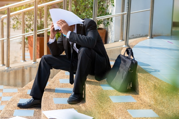 Asiatische Menschen arbeitsloser Geschäftsmann Stress sitzen auf der Treppe, Konzept des Unternehmensversagens und Arbeitslosigkeit Problem aufgrund der globalen Auswirkungen von COVID-19.