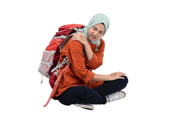 Asiatische muslimische Frau in einem Kopftuch, die mit einem Rucksack sitzt und Rückenschmerzen verspürt