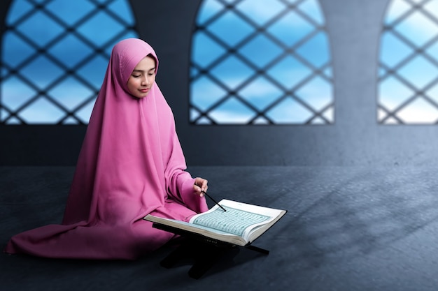 Asiatische muslimische Frau in einem Schleier, der den Koran auf der Moschee sitzt und liest