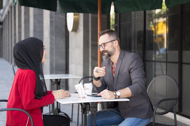 Asiatische muslimische Geschäftsfrau im Coffeeshop im Gespräch mit Kunde oder Freund