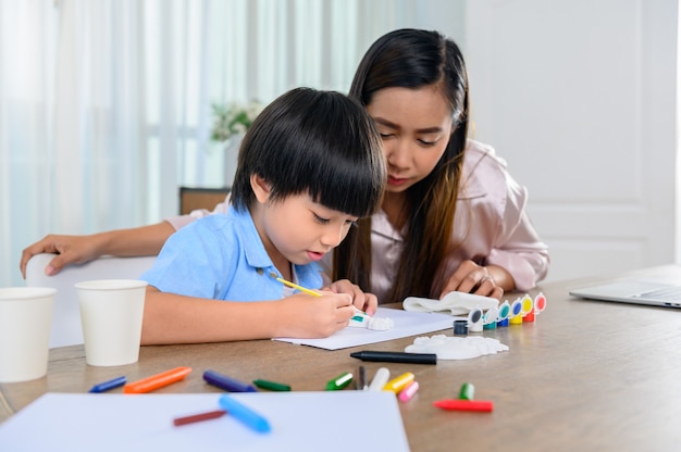 Asiatische Mutter arbeitet nach Hause zusammen mit Sohn. Mutter und Kind zeichnen Bild- und Farbmalerei-Kunst. Frauenlebensstil und Familienaktivität.