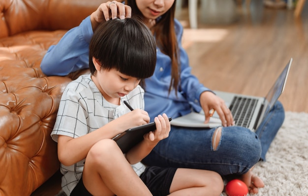 Asiatische Mutter arbeitet nach Hause zusammen mit Sohn. Mutter unterrichtet Kind für Online-Lernausbildung. Neuer normaler Lebensstil und Familienaktivität.