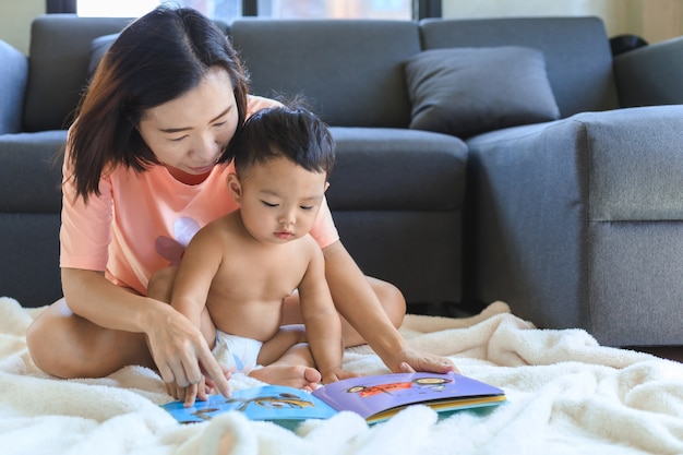 Asiatische Mutter, die Buch mit ihrem niedlichen Baby zu Hause unterrichtet und liest. Familien- und Zusammengehörigkeitskonzept