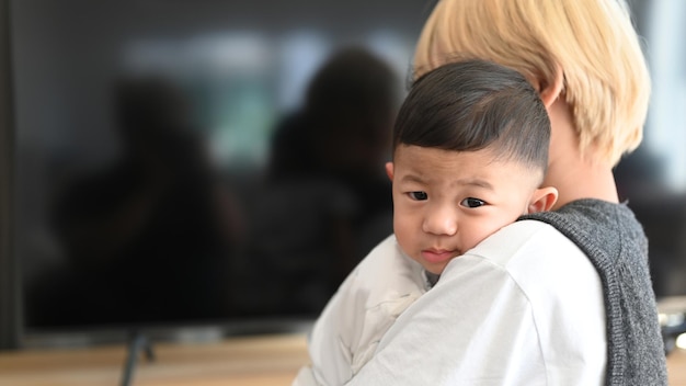 Asiatische Mutter, die ihr Baby zu Hause im Wohnzimmer hält.