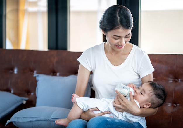 Asiatische Mutter, die ihrem Baby Milch durch Flasche füttert