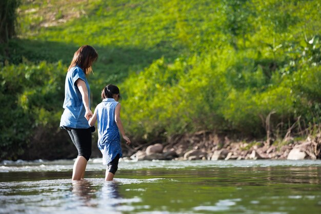 Asiatische Mutter hält ihre Kinderhand, um zusammen im Fluss zu gehen und zu spielen