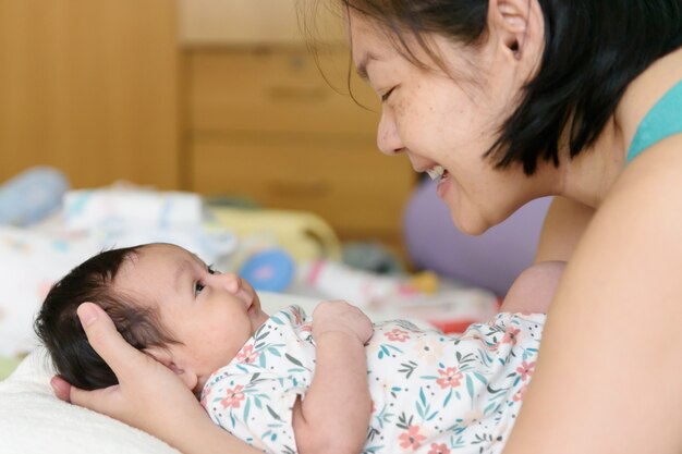 Asiatische Mutter Hände um eine kleine Tochter, die im Bett liegt Lächeln Sie und schauen Sie sich an