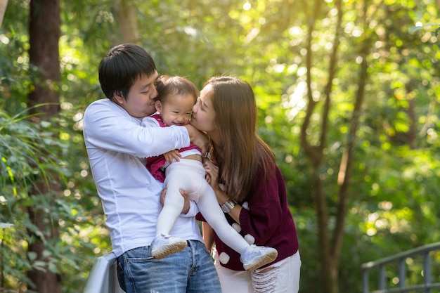 Asiatische Mutter mit Vater, der Tochter im Wald-, Familien- und Liebeskonzept trägt und küsst