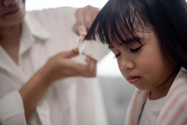 Asiatische Mutter schneidet ihrer Tochter im Wohnzimmer zu Hause Haare, während sie während der Sperrung vor Covid19 Coronavirus sicher zu Hause bleibt Selbstquarantäne und soziales Distanzierungskonzept