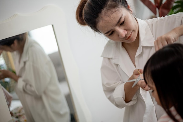 Asiatische Mutter schneidet ihrer Tochter im Wohnzimmer zu Hause Haare, während sie während der Sperrung vor Covid19 Coronavirus sicher zu Hause bleibt Selbstquarantäne und soziales Distanzierungskonzept