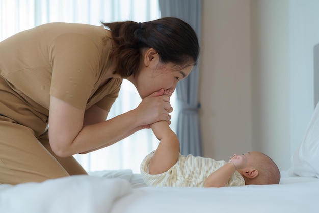 Asiatische Mutter spielt mit ihrem Neugeborenen im heimischen Schlafzimmer, um familiäre Beziehungen und eine gute Entwicklung des Babys zu fördern