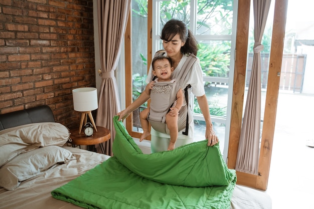 Asiatische Mutter und ihr Baby putzen und arrangieren Decke auf dem Bett