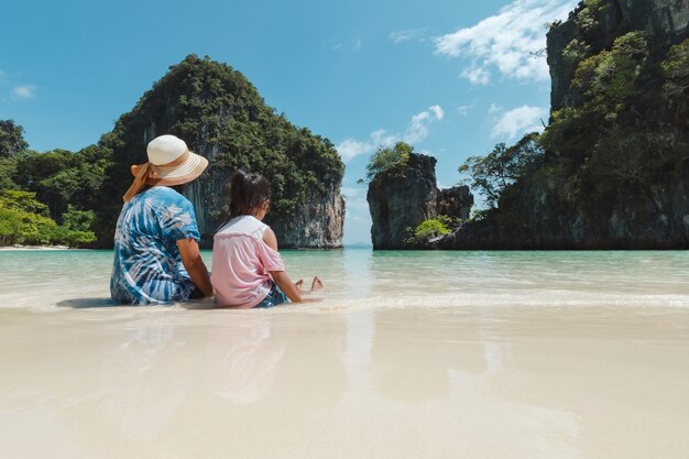 Asiatische Mutter und Kind Mädchen sitzen am Strand.