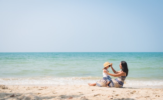 Asiatische Mutter und Tochter sitzen und spielen zusammen am Strand