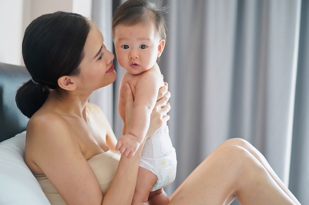 Asiatische Mutter wird ihr Kind Wange mit Liebem Gefühl zu küssen.