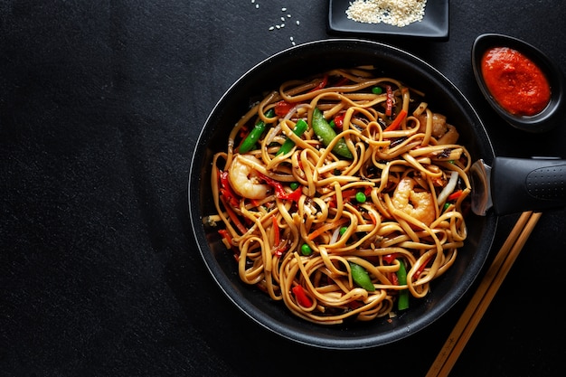 Asiatische Nudeln mit Garnelen und Gemüse serviert auf Pfanne auf dunklem Hintergrund.