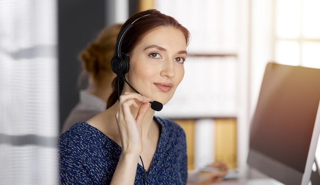 Asiatische oder lateinamerikanische Geschäftsfrau, die per Headset im sonnigen Büro spricht Call Center