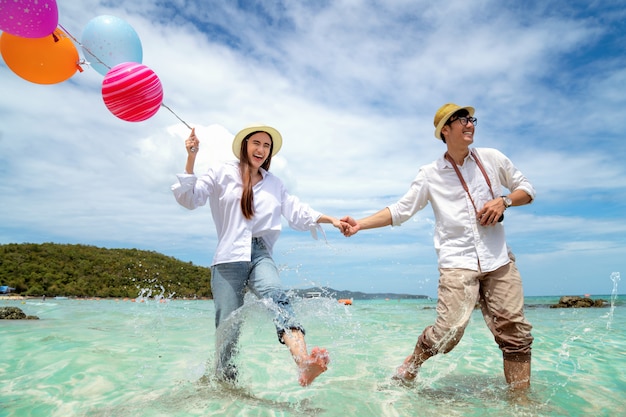 Asiatische Paare laufen und glücklich auf Pattaya-Strand mit Ballon an Hand